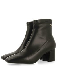 Botas ankle negras hechas de cuero suave, con puntera afilada, tacón cuadrado y un diseño minimalista con costuras sutiles.
