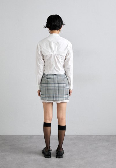 White button-up shirt with a fitted design, gray plaid mini skirt, black knee-high socks, and black shoes. Back view of the outfit.