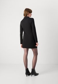 Vestido preto de manga longa com corte reto, apresentando um colarinho e textura suave. Combinado com meias-calças transparentes e botas de tornozelo de bico fino.