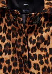 Leopardi-kuosisesti kangastakki, jossa on musta napin sulkeminen ja viilto-olka, pehmeä tekstuuri ja voimakas eläinkuvio.