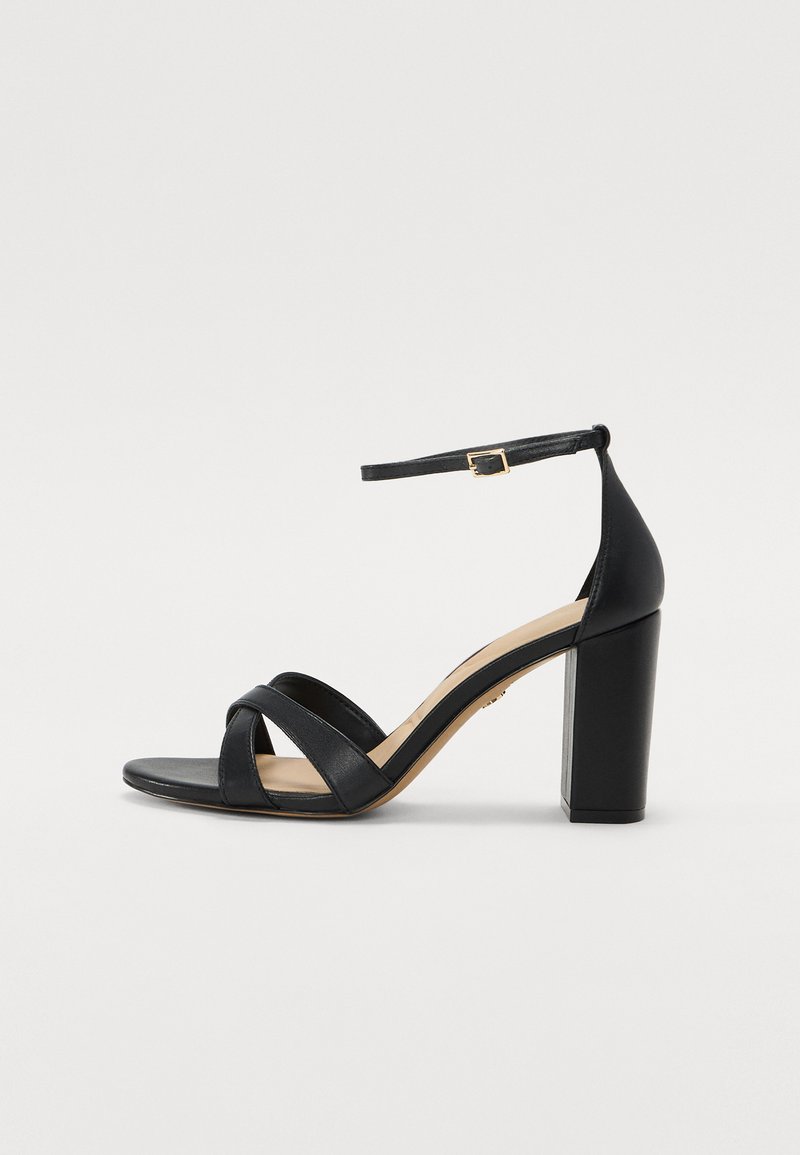 Mustikkamusta nahkakengät korkealla korolla, jossa on tukijalka, nilkkaremmi soljella ja ristikkäiset etuvarpaat. Sujuva pinta ja minimalistinen muotoilu.