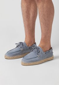 Espadrilles en suède bleu clair avec une semelle en jute naturel, dotées de lacets et de coutures contrastées. Design à dos ouvert pour un enfilage facile.