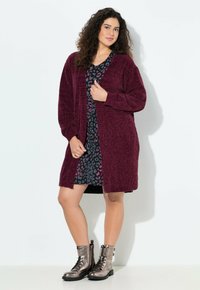 Burgundy texturerad cardigan med öppen framsida, i kombination med en mönstrad svart klänning med rosa accenter, och glänsande metalliska snörstövlar.