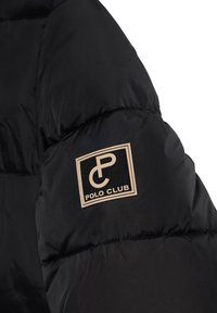 Svart puffjacka med kviltad textur, med en beige rektangulär logotyp som sitter på överarmen och visar "POLO CLUB."