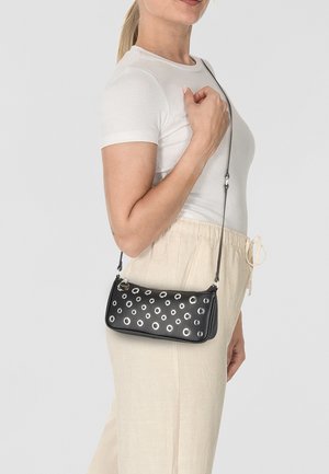 Schwarze Leder-Crossbody-Tasche mit silbernen Ösenakzenten, rechteckiger Form und Reißverschluss. Abnehmbarer verstellbarer Trageriemen für vielseitiges Tragen.