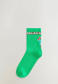 Grøn ankelstrømpe med rød og hvid "FALALA" tekst nær kanten og et lille delvist sukkertøjsstænger- og blåt karakterdesign på siden.