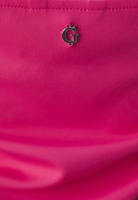 Pink fabric features a smooth texture with a small metallic "G" logo attached, positioned near the top.