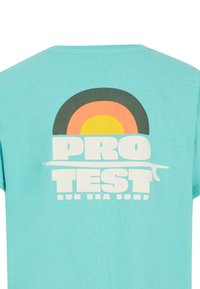 Tyrkysové tričko s grafickým designem s koncentrovanými kruhy v oranžové, žluté a černé barvě, s tučným bílým textem "PRO TEST SUN SEA SURF."