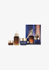 Set med fyra hudvårdsprodukter från Estée Lauder i glasburkar och flaskor. Färgerna inkluderar brunt, blått och guld. Innehåller en reklamboxdesign.