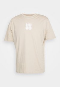 Beige bavlněné tričko s krátkými rukávy a kulatým výstřihem. Na přední straně se nachází bílé logo "HU GO", má hladkou texturu a volný střih.