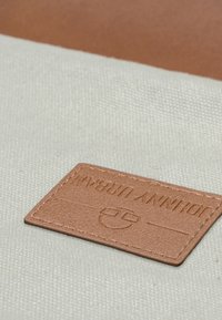 Kangas vaaleassa norsunluussa, jossa on ruskea nahkaleima, johon on painettu "JOHNNY URBAN" ja logo, jos pinnassa on tekstuuria ja suorat reunat.