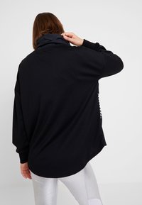 Černý svetr s vysokým límcem, volného střihu a dlouhými rukávy. Má hladkou texturu a minimalistický design.