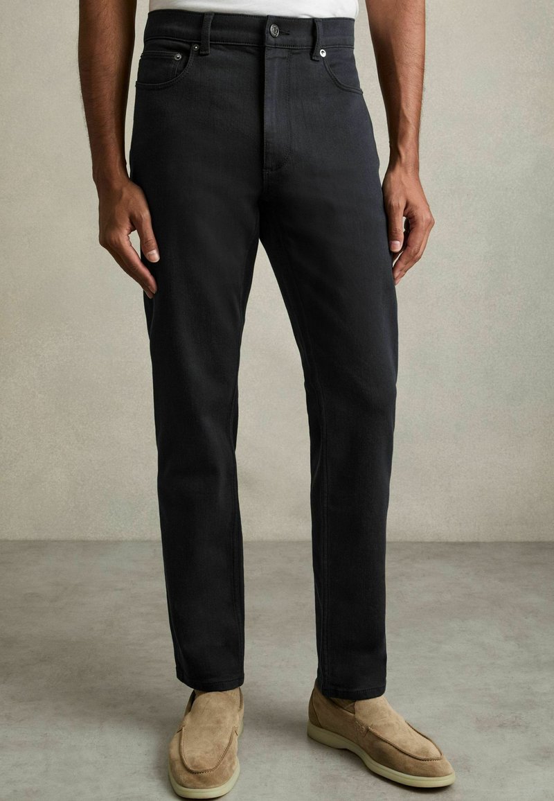 Blugi din denim negru, cu o croială dreaptă, design clasic cu cinci buzunare și închidere cu buton metalic. Purtați cu încălțăminte de culoare deschisă.