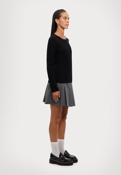 Black ribbed sweater, gray pleated skirt, and black platform loafers with a thick sole. Model wears white crew socks, hair in braids.