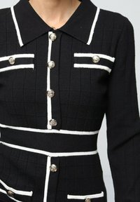 Robe en maille noire avec des accents blancs, présentant un col, un design structuré, un tissu texturé et des détails de boutons en argent.