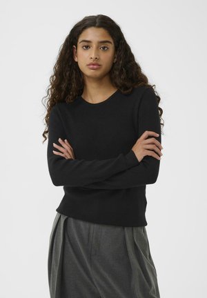 Black ribbed long-sleeve sweater with a round neckline, fitted silhouette, and textured fabric. Paired with gray pleated trousers.