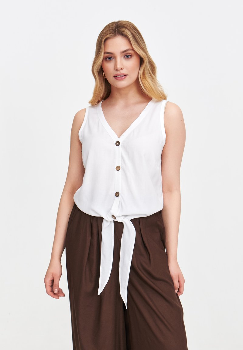 Biała bezrękawnikowa bluzka z dekoltem w kształcie litery V i trzema brązowymi guzikami, z wiązaniem z przodu. Gładki materiał, luźny krój i lekka konstrukcja.