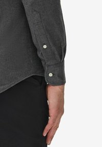 Grå skjorta med knäppning och långa ärmar, med en strukturerad väv, spetsiga manschetter och kontrasterande ljusa knappar. Svart tyg under.