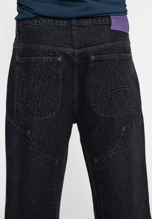 Los jeans de mezclilla negra cuentan con dos bolsillos traseros con letras bordadas en relieve "M" y "A". Una etiqueta de marca púrpura está cosida en la cintura.