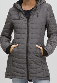 Grå vadderad jacka med quiltad design, justerbar huva, framdragkedja och sidofickor; svarta ribbade muddar vid ärmarna.