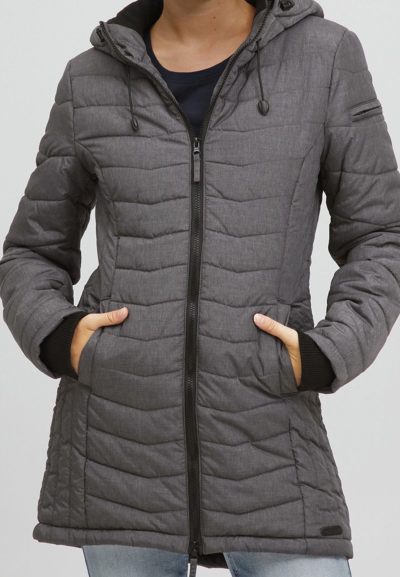 Grå vadderad jacka med quiltad design, justerbar huva, framdragkedja och sidofickor; svarta ribbade muddar vid ärmarna.