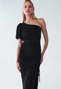 Schwarzes One-Shoulder-Kleid mit einer figurbetonten Silhouette, gerafften Seitendetails und Zugbandakzent. Weicher Stoff und strukturierte Oberfläche.