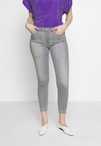 Grå hög midja skinny jeans med texturerad yta, i kombination med en ljuslila topp och vita platta skor.