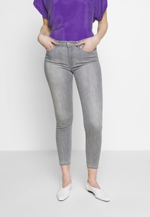 Jeans ajustados de talle alto grises con un acabado texturizado, combinados con una blusa púrpura brillante y zapatos planos blancos.