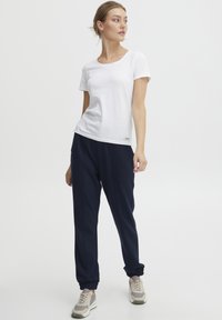 Vit kortärmad t-shirt kombinerad med marinblå joggers. Joggers har elastiska manschetter och sido sömmar. Modellen bär ljusa sneakers.