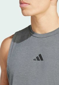 Haut de sport sans manches gris en tissu doux ; présente un logo triangulaire noir sur la poitrine et un col arrondi.