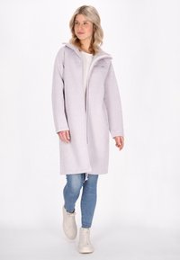 Manteau long en polaire lavande clair avec fermeture éclair devant, capuche et ourlet à cordon ; porté par-dessus une chemise blanche et un jean bleu, associé à des baskets claires.