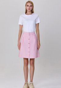 Jupe A-line à rayures roses et blanches avec taille haute, fermeture à boutons sur le devant et poches latérales, associée à un t-shirt blanc uni.