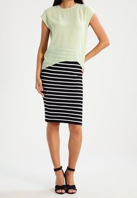 Ljust grön, kortärmad, genomskinlig blus i kombination med en svart och vit randig pennkjol. Svarta sandaler med ankelsnörning fulländar looken.