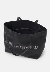 Zwarte leren shopper met twee handvatten, voorzien van een zilveren gestikte logo aan de voorkant. De binnenkant bevat een ritsvak voor veilige opberging.