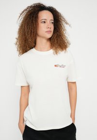 Bílé bavlněné tričko s kulatým výstřihem a krátkými rukávy. Na levé straně hrudi je vícebarevná květinová výšivka. Volný střih.