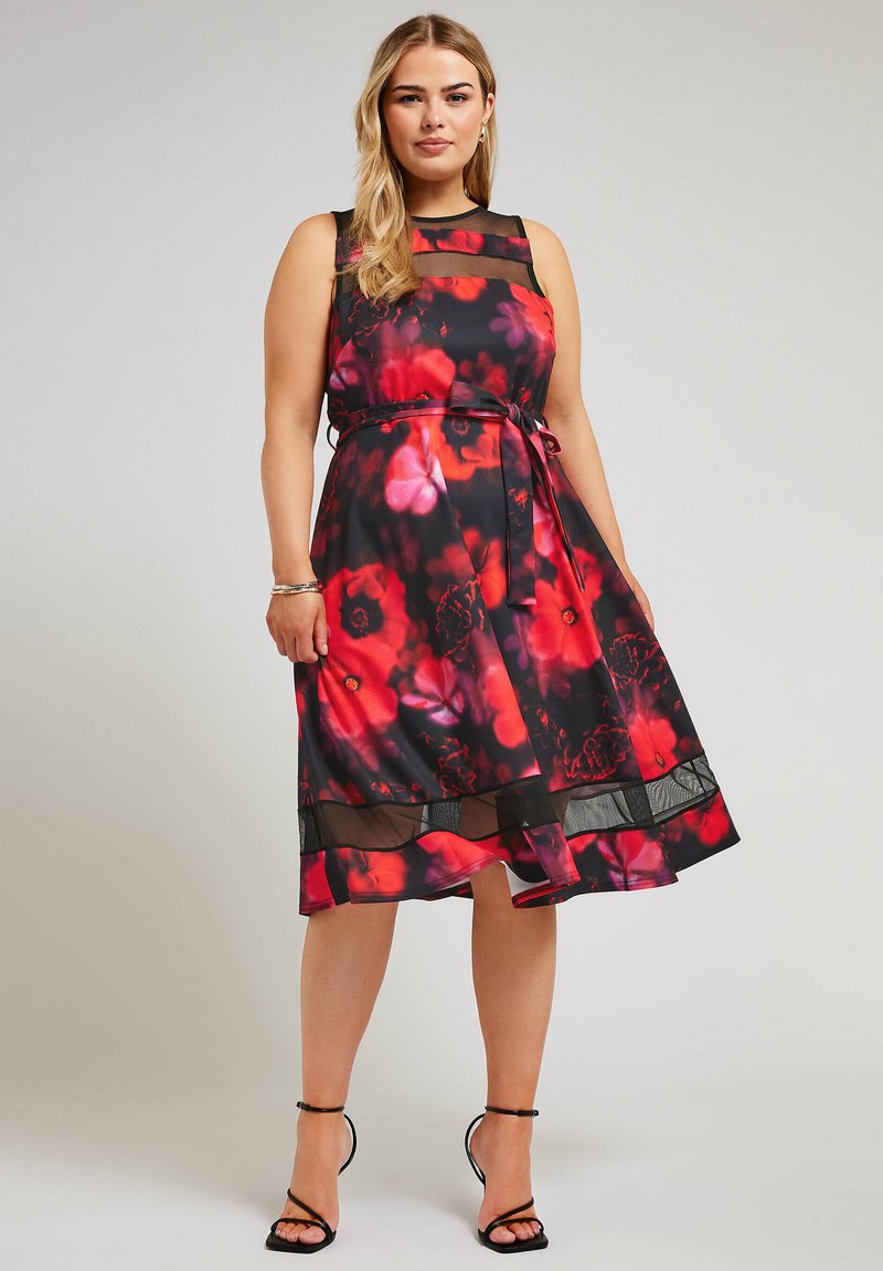 Vestido negro con un patrón floral en rojo y rosa, detalles de malla, cintura ajustada y dobladillo acampanado con una superposición transparente.