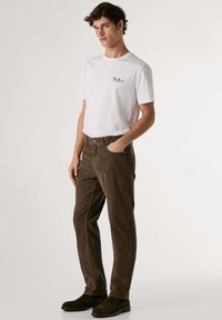 Camiseta blanca de cuello redondo con un pequeño logo azul, combinada con pantalones de pana marrones y botas de tobillo marrones oscuras. Un look sencillo y casual.