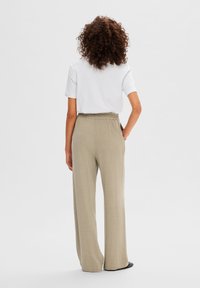 Witte T-shirt gecombineerd met losse, beige wijdlopers met een elastische tailleband. Gladde stof met een lichte glans.