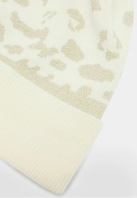 Crème gebreide beanie met een metallic gouden luipaardprint en een geribde manchette onderaan voor extra textuur en detail.