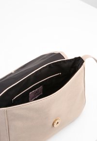 Beżowa skórzana torebka o fakturowanej powierzchni, zapięciem na złoty zatrzask oraz czarnym materiałowym wnętrzem wyposażonym w jedną kieszeń na suwak.
