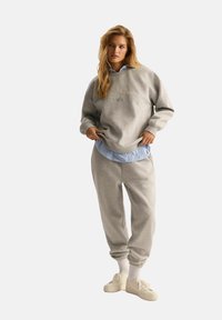 Szara bawełniana bluza i pasujące dresowe spodnie w skrojonym, warstwowym stylu na niebiesko-pasiastą koszulę. Białe sneakersy dopełniają stylizację.