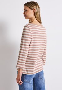 Gestreepte langarmtop in zacht roze en crème, met een bootneck en een ontspannen pasvorm, gecombineerd met lichtblauwe denimjeans.