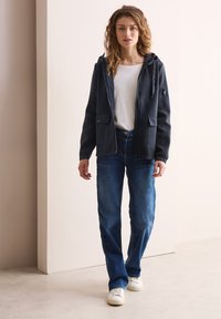 Sweat à zip bleu marine avec poches latérales, associé à un jean droit bleu clair et des baskets blanches. Texture lisse, design décontracté.