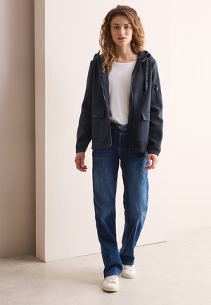 Sudadera con cremallera color navy y bolsillos laterales, combinada con jeans rectos azul claro y zapatillas blancas. Textura suave, diseño casual.