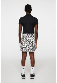 Svart pikétröja med korta ärmar, i kombination med en vit kjol med svart zebratäckesmönster. Silverlogotyp på tröjans baksida.