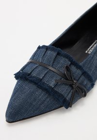 Jeans flat sko i mørk marineblå, med spiss tå og frayed detaljer. Har en svart båndsløyfe og teksturert overflatedesign.