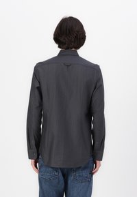 Gray long-sleeve shirt with vertical stripes, featuring a pointed collar, button cuffs, and a back shoulder loop detail. Worn with blue jeans.