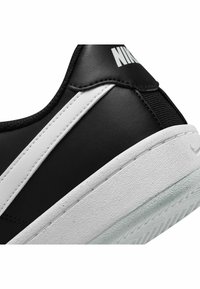 Sneaker nera con striscia in pelle bianca, suola in gomma texturizzata e branding in rilievo. Presenta una forma arrotondata e collarino imbottito.