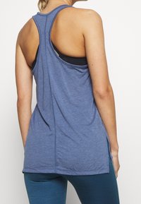 Top atletico senza maniche di colore blu con design racerback, caratterizzato da una texture morbida e fessure laterali per un movimento migliorato.