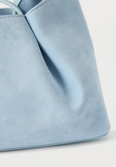 Ελαφρύ μπλε σουέντ τσάντα χειρός με απαλή υφή και ελάχιστες εμφανείς ραφές σε λευκό φόντο.